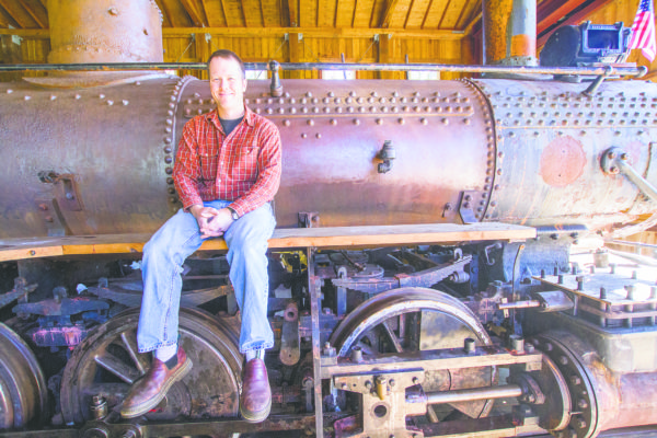(Kyle Mittan | The Daily World) Polson Museum Director John Larson sits on the running board of the Polson No. 45, a logging locomotive that once transported logs around the Harbor in the early-to-mid 1900s.