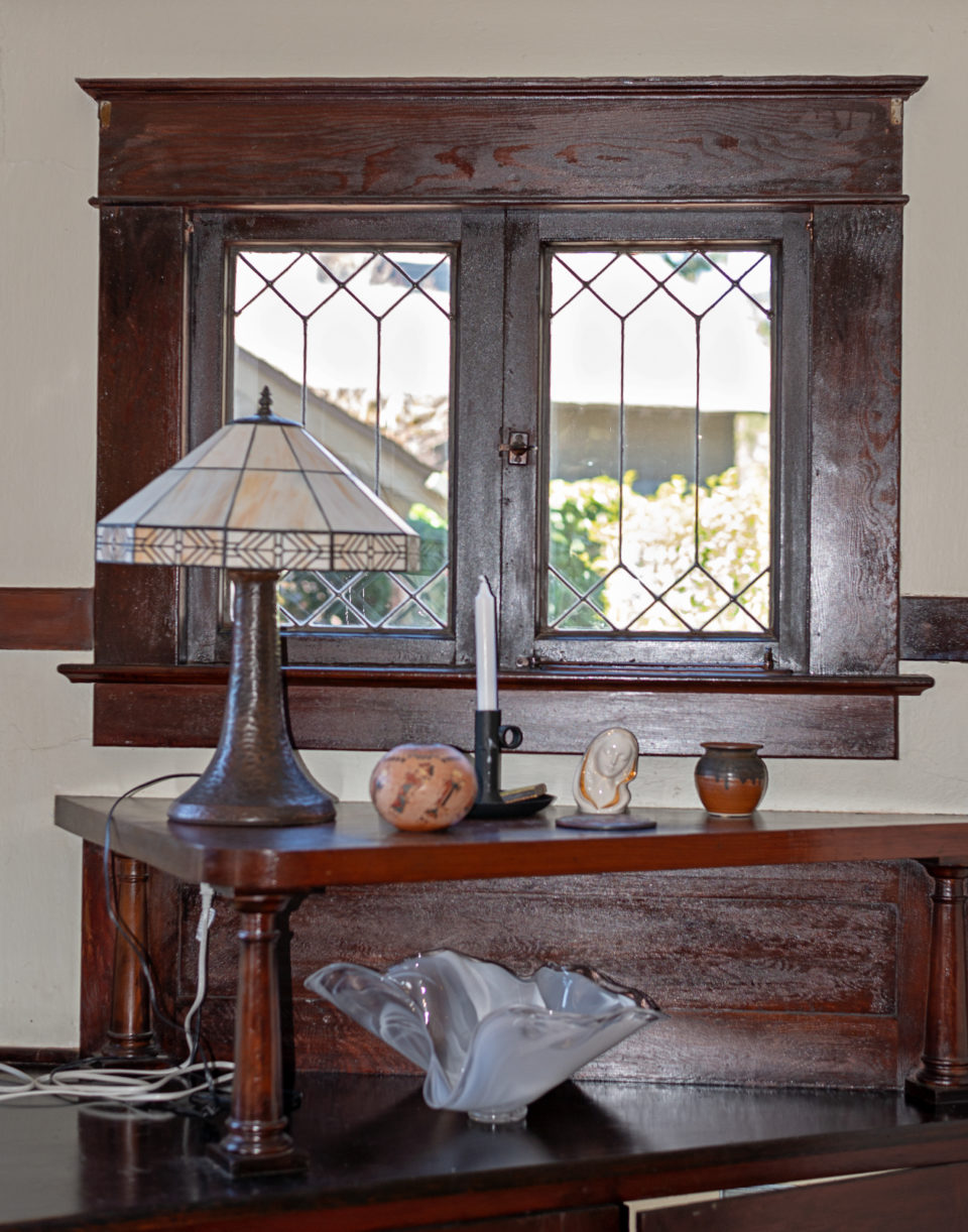 The original Craftsman-style woodwork has been left unpainted in much of the house. Below this window is a large bank of built-in cabinetry in a room that may have originally been a formal dining room.